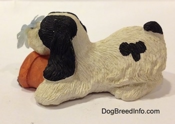 The left side of a sandicast black and white American Cocker Spaniel dog that is sniffing a flower out of a knocked over pot figurine.