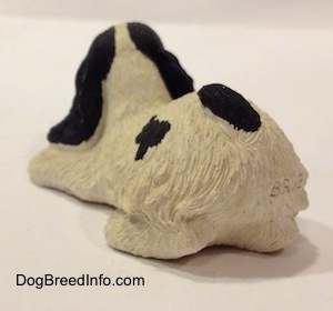 The back left side of a sandicast black and white American Cocker Spaniel that is sniffing a flower out of a knocked over pot figurine. The figurine does not have a tail.