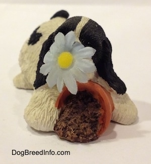 A sandicast black and white American Cocker Spaniel that is sniffing a flower out of a knocked over pot figurine. The flower on the figurine is made of a cloth.