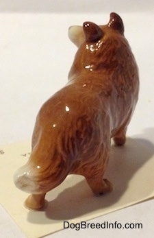 The back right side of a brown with white Collie dog figurine. The figurine is glossy,