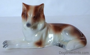 The left side of a brown and white Collie dog figurine in a lying down pose. The figurine has small black eyes for circles.
