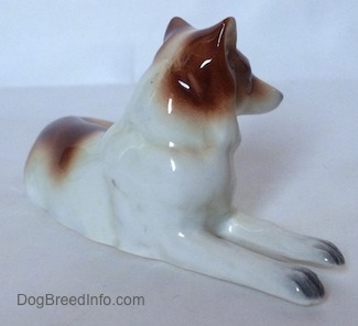 The front right side of a brown and white Collie dog figurien that is in a lying down pose. The figurine is glossy.