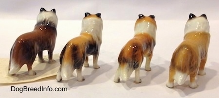 The back right side of four Collie dog figurine variations. The tips of each of the figurines tails are black.