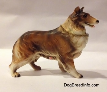 The right side of a ceramic Rough Collie figurine that is brown, black and white. There is a sticker on the side of a figurine.