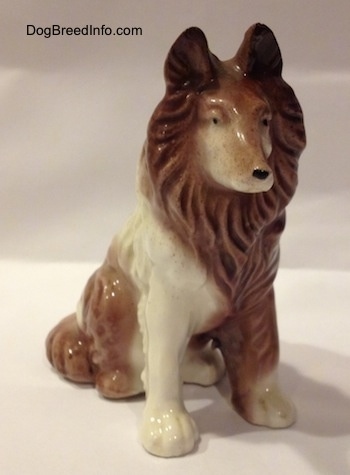 A brown and white porcelain Rough Collie figurine in a sitting pose. The figurine has black circles for eyes.