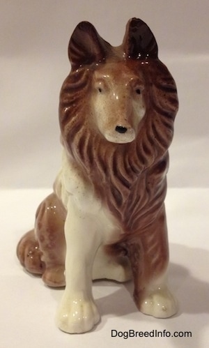 A brown and white porcelain Rough Collie figurine that is in a sitting pose. The figurine has its ears up.