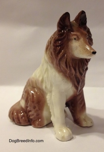 The front right side of a figurine that is a brown and white porcelain Rough Collie in a sitting pose. The figurine has fine paw details.