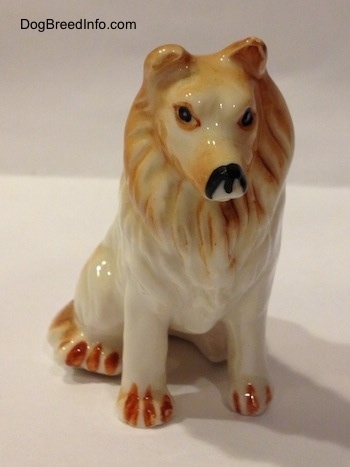 A tan and white bone china Rough Collie figurine. The figurine has poor facial details.