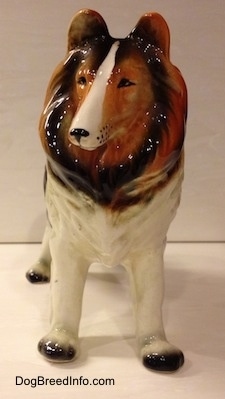 A black, brown and white highly detailed ceramic Rough Collie figurine. The figurine has black whisker dots around its muzzle.