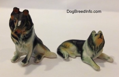 Two Rough Collie figurines, one is in sitting position and the other is lying down.