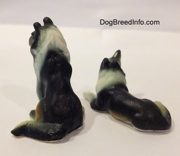 The back of two Rough Collie bone china figurines, one is sitting and the other is lying down and looking up.