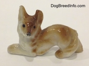 The left side of a bone china Coyote figurine in a play bow pose. The figurine has black circles for eyes.