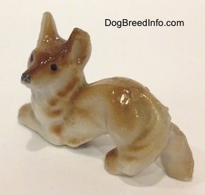 The front left side of a bone china that is a tan and white Coyote figurine in a play bow pose. The figurine has chipped ears.