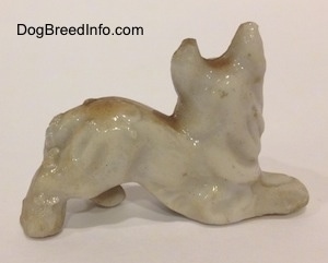 The right side of a tan and white bone china Coyote figurine in a play bow pose.