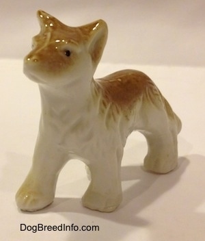 The front left side of a bone china figurine that is a tan and white Coyote figurine. The figurine has black circles for eyes.