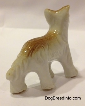 The front right side of a bone china tan and white Coyote figurine in a standing pose. It is hard to differentiate the tail from the body of the figurine.