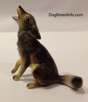 The left side of a black, tan and white Coyote figutine that is in a howling pose. The figurine has fine eye details.