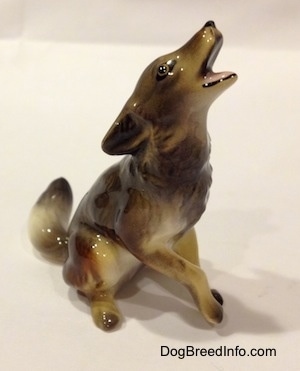 The front right side of a black, tan and white Coyote figurine in a howling pose. The animal has its mouth open.