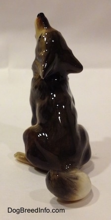 The back of a black, tan and white Coyote figurine that is in a howling pose. The figurine has a long tail.