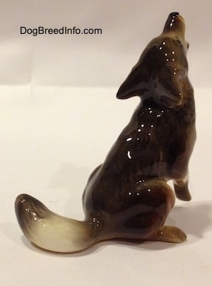 The back right side of a figurine that is a black, tan and white Coyote figurine that is in a howling pose. The figurine is glossy.