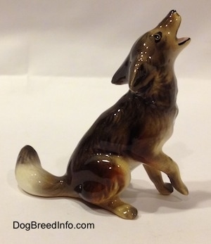 The right side of a figurine that is a black, tan and white Coyote in a howling pose.The figurine is glossy.