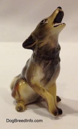 The front right side of a black, tan and white Coyote figurine in a howling pose. The figurine has its front left paw slightly up.