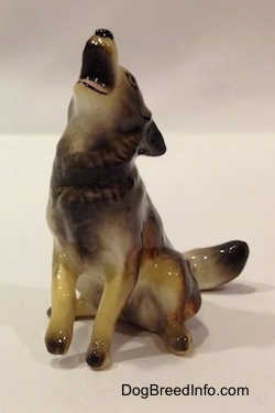 A figurine of a black, tan and white Coyote figurine that is in a howling pose. The figurine has black on the tip of its paws.