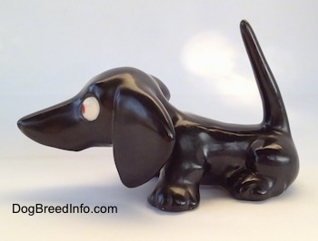 The left side of a black Dachshund figurine. The figurine has a very long tail that is in the air.