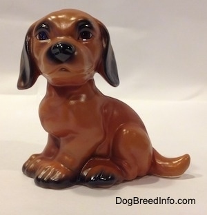 The left side of a brown with black Dachshund puppy in a sitting pose figurine. The figurine has large eyebrows.