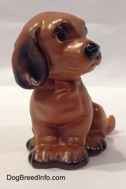 A brown with black Dachshund puppy in a sitting pose figurine. The figurines paws are connected together.