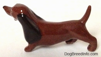 The left side of a brown Dachshund figurine. The figurine has long ears that are on its side.