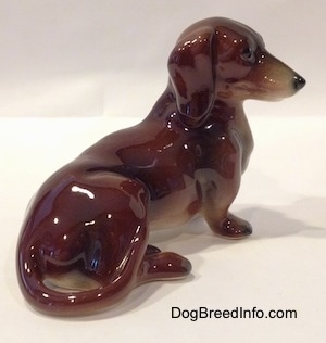 The right side of a figurine of a brown and black Dachshund in a sitting pose. The figurine has a detailed face.