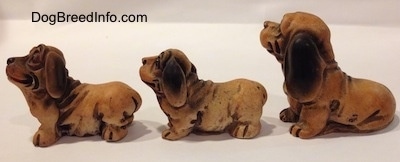 The left side of three different cartoon like plastic Dachshund figurines. All of the figurines have large paws and short legs.