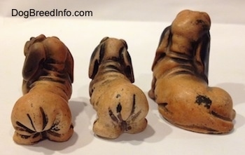 The backside of three different plastics Dachshund figurines that have cartoon like features. Two of the three figurines lack paw details..