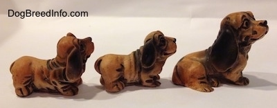 The right side of three different plastic cartoon like Dachshund figurines. The figurines are varying in sizes.