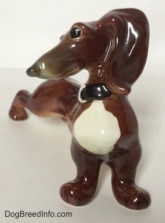A brown with white Dachshund figurine in a strecthing pose. The figurine has big black circles for eyes.