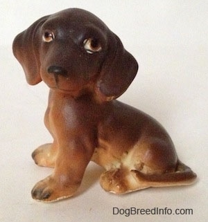 The left side of a brown with tan Dachshund puppy in a sitting pose figurine. The figurine has big ears.