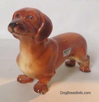The front left side of a brown Dachshund figurine that is in a standing pose. The figurine has great face details.