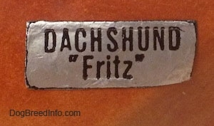 Close up - A sticker on the side of a Dachshund figurine that reads - DACHSHUND 'Fritz'