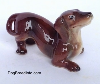 The front right side of a figurine that is of a brown with tan Dachshund in a play bow pose. The figurine has black circles for eyes.