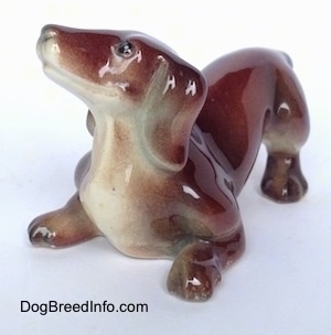 A figurine that is a brown with tan Dachshund in a play bow pose.