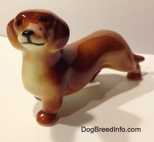 The front left side of a figurine of a brown Dachshund. The figurine has small black circles for eyes.
