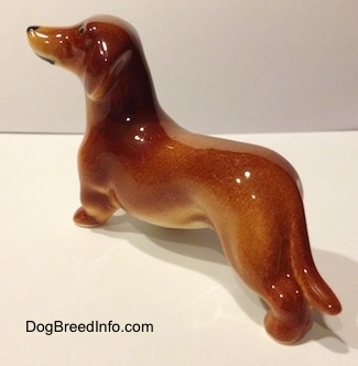 The back left side of a brown Dachshund figurine. The figurine is glossy.