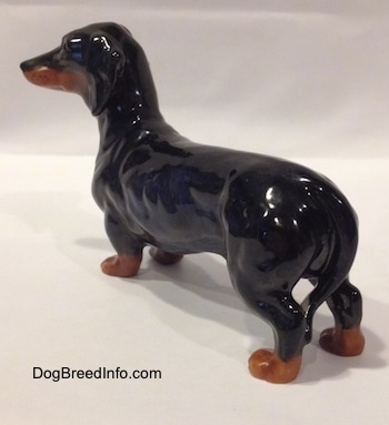 The back left side of a black and brown Dachshund figurine. The figurine has brown paws with black nails.