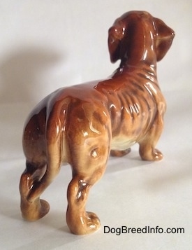 The back right side of a brown Dachshund figurine. The figurine has short detailed legs and paws.