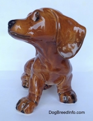 A figurine of a brown Dachshund puppy figurine that is in a sitting pose. The figurine has long ears.