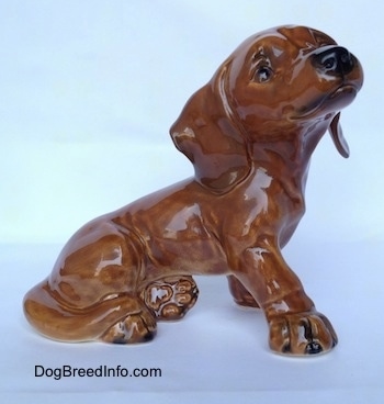 The right side of a brown Dachsund puppy figurine in a sitting pose. The figurine has fine paw details and it has black nails.