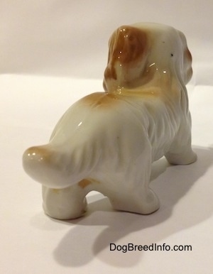 The back right side of a figurine that is a white with tan long haired porcelain Dachshund. The figurine has a long tail with hair details on it.
