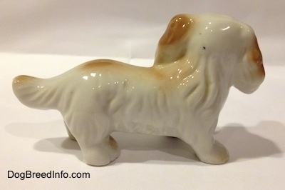 The right side of a white with tan porcelain long haired Dachshund figurine. The figurine has big ears with hair details.
