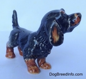 The front right side of a black and brown Dachshund figurine in a standing pose with its tail up. The figurine has a long ear with brown on it.